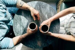 Couple sitting at a table drinking coffe not talking representing a couple that has diconnected from each other. If you and your partner have diconnected and lost intimacy in your relationship there is hope. Online couples counseling in Texas can help you reconnect and strengthen your bond. 