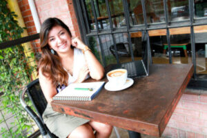 Priscilla Rodriguez of Modern Wellness Counseling sits at a table smiling while having coffee. Modern Wellness offers Online Therapy for different types of Trauma in San Antonio, TX.