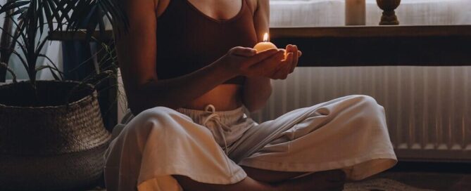 Woman meditating on the floor in the lotus position with a small tea light in her hand representing someone who is using the skills developed during Therapy for Anxiety in San Antonio, TX to find calm.