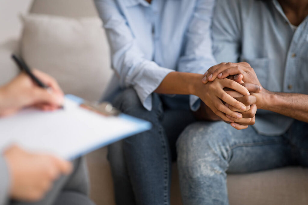 Couple sitting together with hands clasped in their therapists office representing a couple who is benefiting from Couples Therapy in San Antonio, TX.