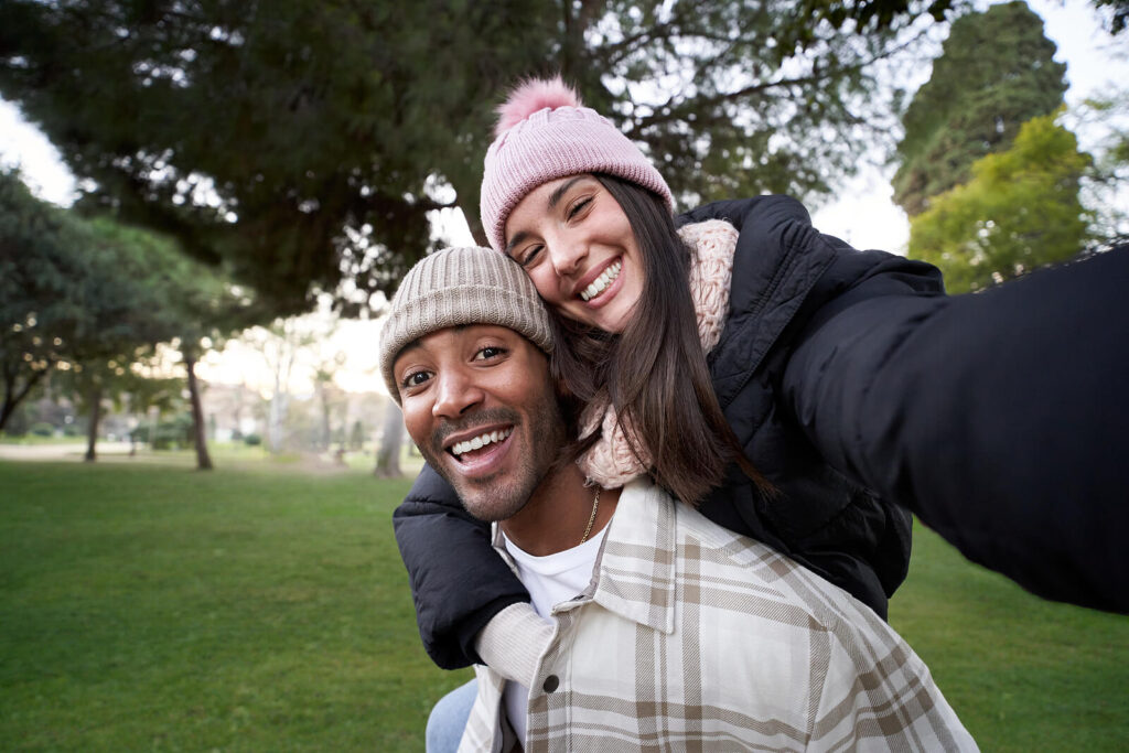 Interracial couple happily interact outside while taking a selfie represents a couple who has overcome anxiety to grow and improve their relationship through Couples Counseling in San Antonio, TX.