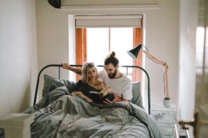 Couple bonding in bed together, enjoying reading in bed together as they are spending quality time. Modern Wellness Counseling, San Antonio, Texas. 78249, 78256, 78230, 78258